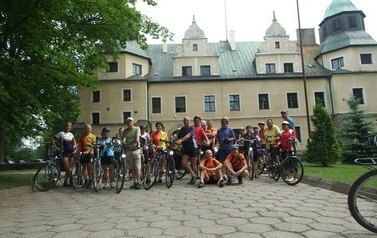 Duża grupa kilkudziesięciu rowerzyst&oacute;w pozuje do grupowego zdjęcia przed zamkiem w Goraju.