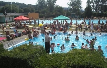 Otwarty basen w Czarnkowie, kilkadziesiąt os&oacute;b kąpie się lub obserwuje kąpiących, z przodu zieleń.